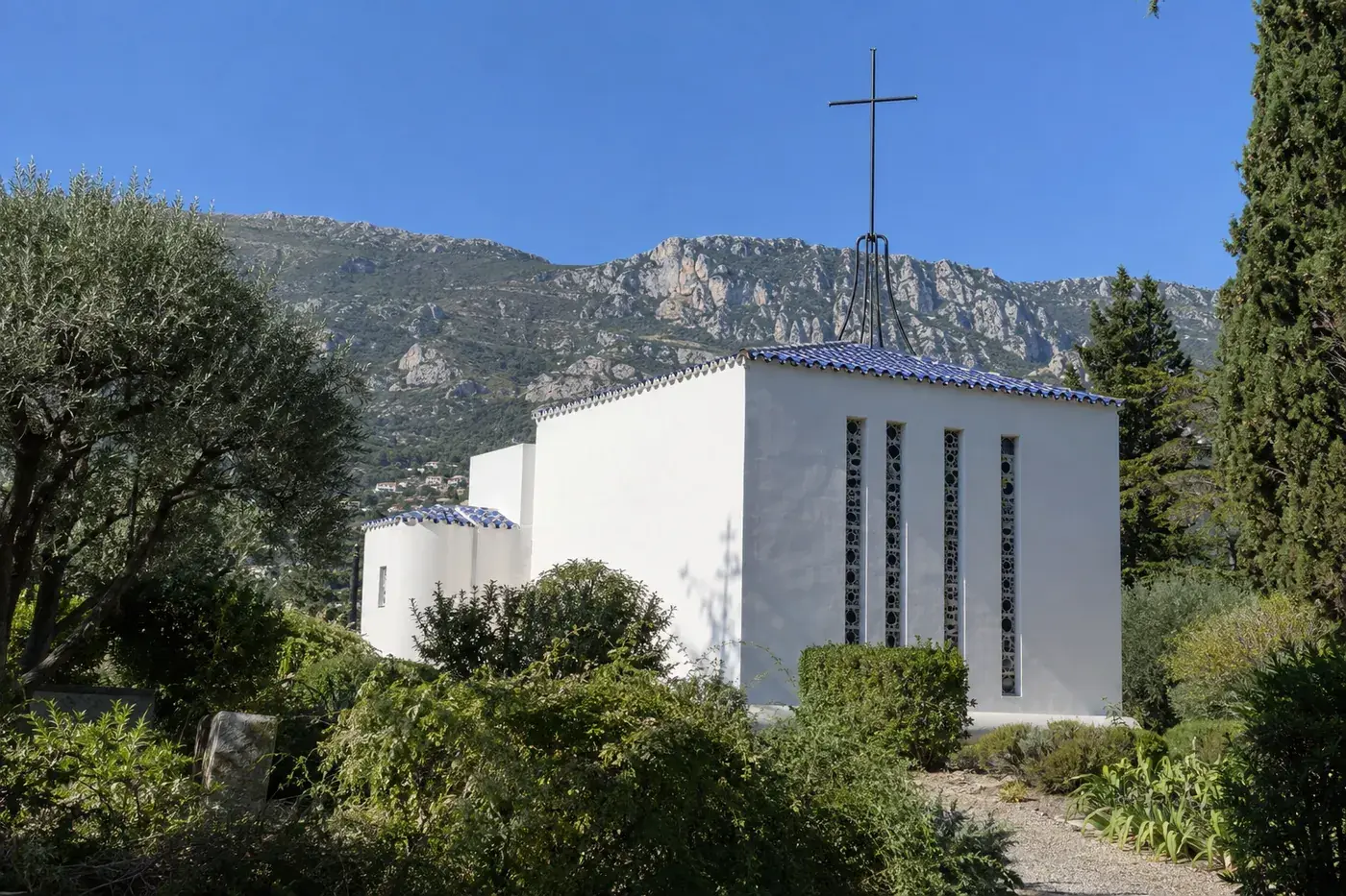 La chapelle du Rosaire à Vence, murs blancs, toit de tuiles bleues et blanches et grande croix de fer forgé