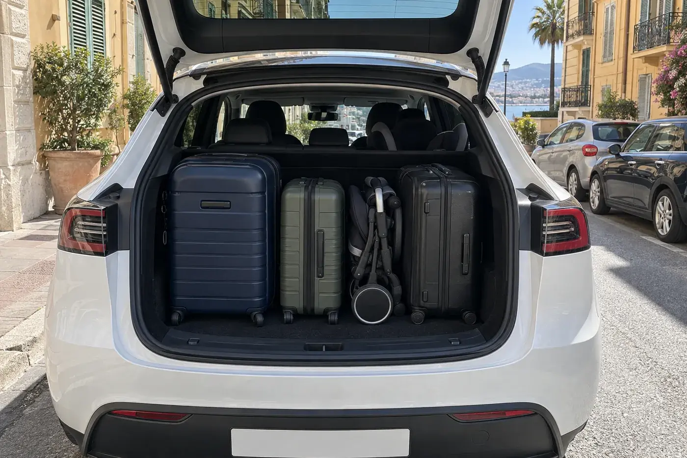 Coffre arrière ouvert d’une Tesla Model Y blanche, avec trois valises et une poussette pliée, dans une rue de Nice