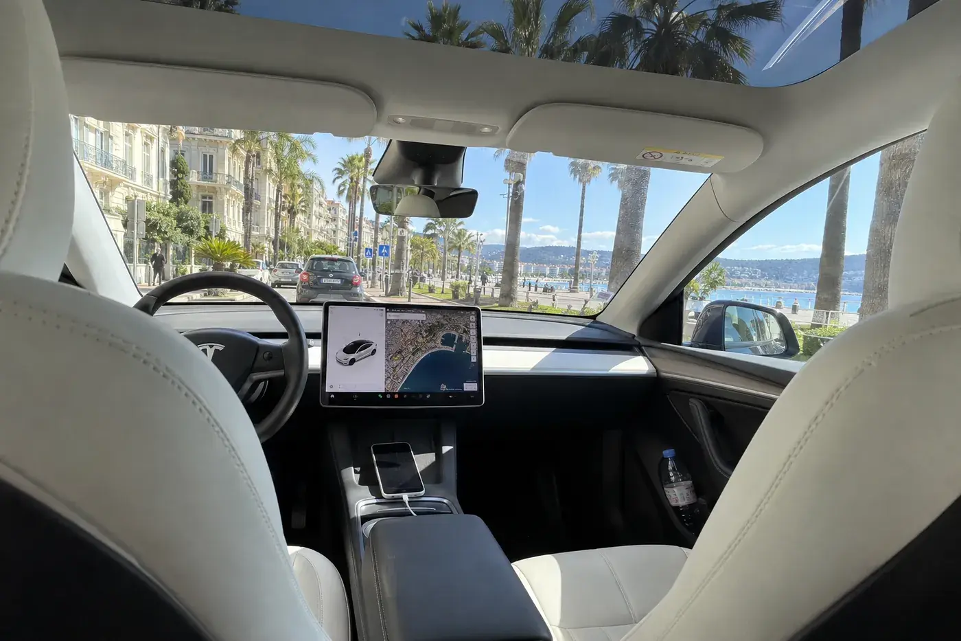 Intérieur d’une Tesla Model Y vu de la banquette arrière : sièges clairs, écran central, toit vitré