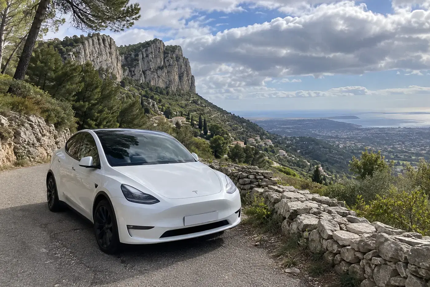 Tesla Model Y blanche sur une petite route au pied des falaises du baou, au-dessus de Vence, la côte au loin